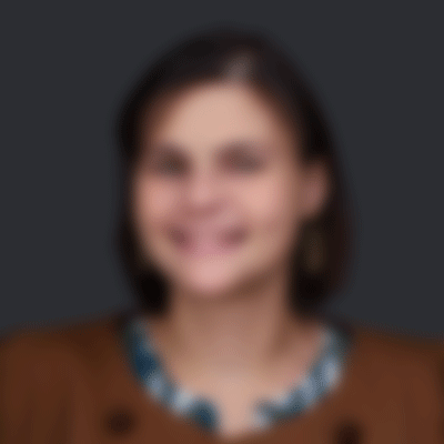 A blurred portrait of a smiling woman with medium-length hair, wearing a brown jacket with a floral pattern underneath.